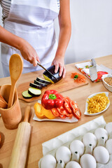 Obraz na płótnie Canvas Female cook cutting eggplant on wooden board in kitchen.