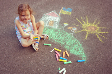 Fototapeta premium Ukrainian girl child draws children's drawings with chalk on the pavement.