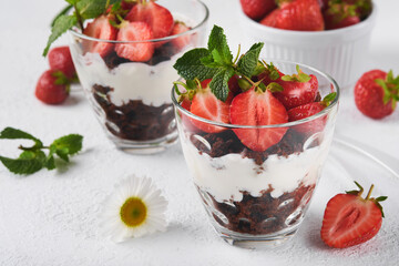 Trifles. Brownies, fresh strawberry and mascarpone cream servered in layers on glass on white background. Portion desserts. No baked brownie cheesecake with fresh berries in a glass.