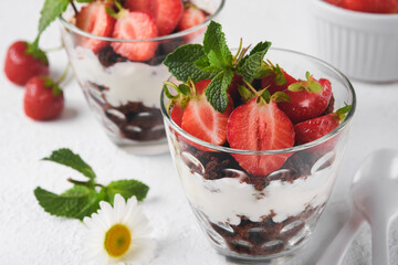 Trifles. Brownies, fresh strawberry and mascarpone cream servered in layers on glass on white background. Portion desserts. No baked brownie cheesecake with fresh berries in a glass.