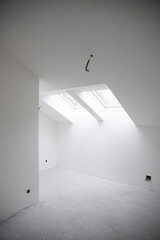 Fototapeta na wymiar modern attic construction site freshly painted, the floor is still screed, walls are white