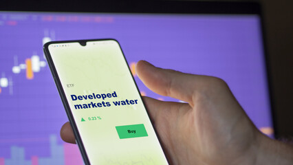 An investor's analyzing the water etf fund on screen. A phone shows the ETF's prices developed markets water to invest