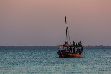 ZANZIBAR, TANZANIA - SEPTEMBER 2019: People on the boat sailing at the sunset in the background of purple sky