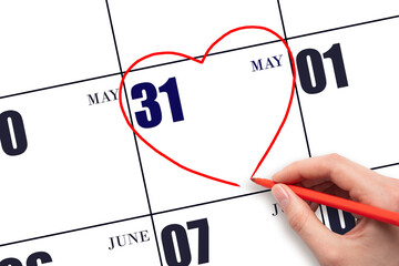 A woman's hand drawing a red heart shape on the calendar date of 31 May. Heart as a symbol of love.