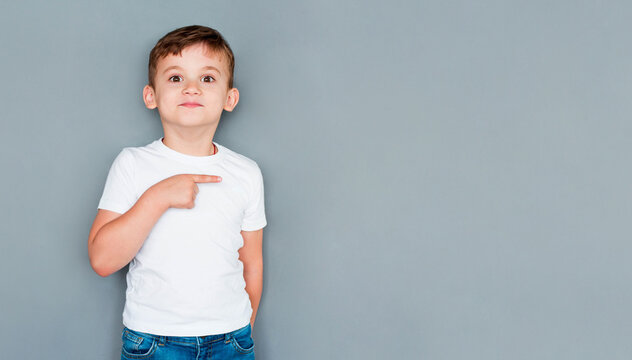 Look, advertise here. Portrait of cute cheerful little boy in white T-shirt pointing to empty place on background, preschooler showing copy space for promotional ad. indoor studio shot
