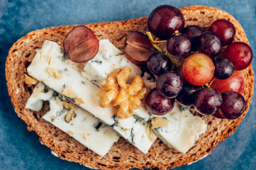 Open sandwich from toasted bread with mild creamy blue cheese, grapes and walnuts on blue plate