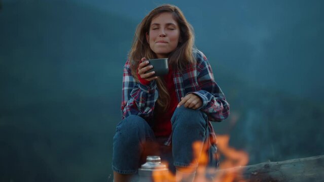 Drinking woman enjoy evening tea by camping fire. Chill girl dream in mountains.