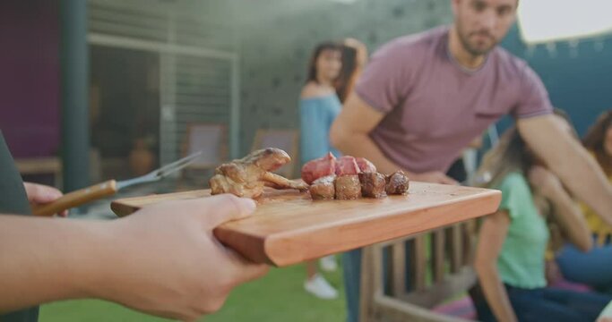 Group of friends having an outdoor barbecue. Man serves meat to friend and sausages. Happy people at home backyard BBQ party celebration