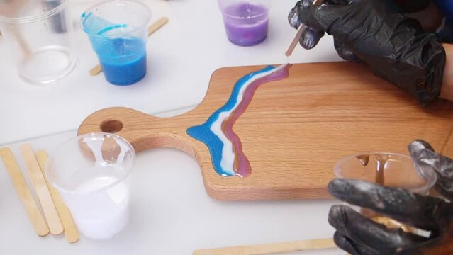 Epoxy resin art. Imitation of the sea. Sea foam. Modern trendy hobby. The pouring process of a wooden. Decorative cutting board. Master carpenter fills a wooden board with epoxy resin. Blue and white