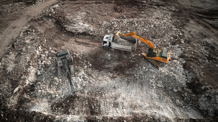 Obraz premium Aerial view of excavator loading tipper truck with crushed rock soil. Machineries at construction site. Earthworks. Heavy machinery at earthmoving works