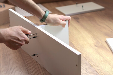 The furniture assembler tightens the cam bolt fixing into the furniture made of particle board with a hex wrench, flat pack furniture assembly.
