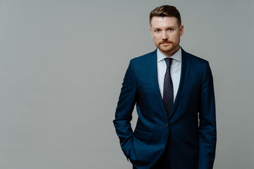 Confident male boss in blue navy suit looking at camera while standing against grey background