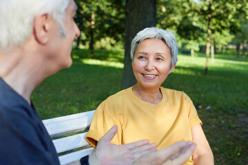 Attractive older couple talking seated on bench in summer park