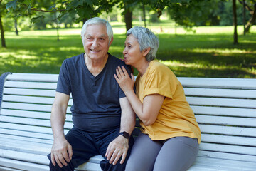 Attractive older couple talking seated on bench in summer park