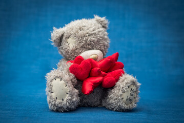 Gray teddy bear with hearts sits on a blue background
