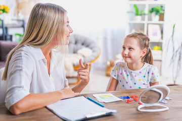 Doctor and small patient train articulation, work on problems and obstacles child with dyslexia. little girl together with speech therapist is sitting at desk indoors, playing game, studying sounds