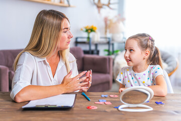 Doctor and small patient train articulation, work on problems and obstacles child with dyslexia. little girl together with speech therapist is sitting at desk indoors, playing game, studying sounds