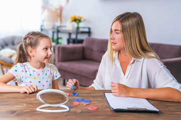 Doctor and small patient train articulation, work on problems and obstacles child with dyslexia. little girl together with speech therapist is sitting at desk indoors, playing game, studying sounds