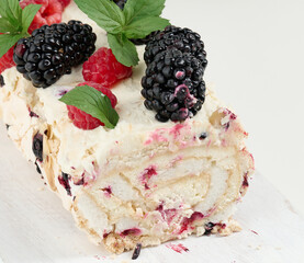 Baked meringue roll with cream and fresh fruits on a white wooden board, delicious dessert