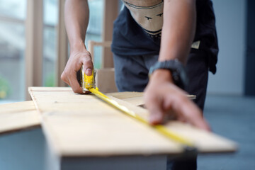 Fototapeta na wymiar Worker measuring the length of a wooden deck with a tape measure in a workshop. Selective focus photo