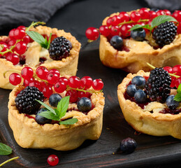 Fruit tart with red currants sprinkled with powdered sugar on a black table