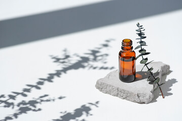 Open amber bottle without cap with eucalyptus branche. White background with daylight and beautiful shadows. Skincare serum or essential oil natural cosmetic. Beauty concept for face and body care