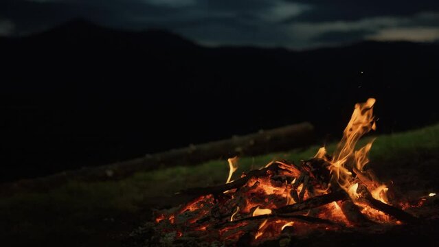 Closeup camp fire burning in dark evening night mountains landscape nature.