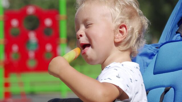 Funny kid making faces while eating popsicle on a summer day, 1.5 year old toddler face closeup.