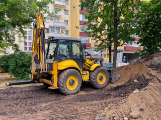 Fototapeta na wymiar bright, yellow excavator digs a hole in the sand. construction machinery. reliable road construction vehicle drives through sand and leaves tire tracks