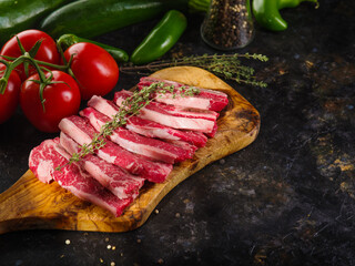 Raw meat steaks with a sprig of rosemary on a wooden cutting board, vegetables on a dark background. Cooking steaks from beef, pork in the home kitchen. Recipe book, food blog.