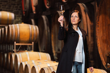 Woman tasting wine at the wine cellar with barrels in background