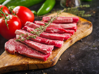 On a wooden cutting board, appetizing meat steaks with a sprig of rosemary, fresh tomatoes, peppers on a dark background. Recipes for meat dishes. Banquet, picnic, family holiday.