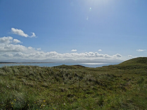 Landscape with rolling green grass, blue sea and clouds over the mountains of Snowdonia, taken from Llanddwyn Island, Newborough, Anglesey