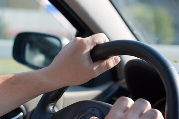 Male hands on the steering wheel of a car close-up.