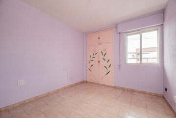 Empty room with purple painted walls, stoneware floor, built-in wardrobe with painted doors and white aluminum window