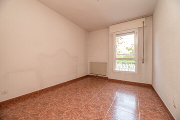Empty living room with reddish stoneware floor, white radiator on the wall and window with view