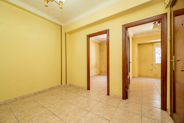 Empty living room with cream stoneware floors, soft yellow walls and reddish woodwork on the doors