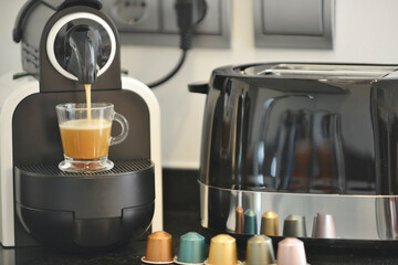 Capsule coffee maker on a black countertop, a plug and a transparent cup filling with coffee