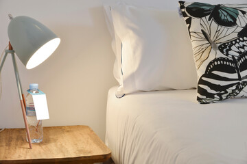 Bedroom with cushions and pillows, white wall, wooden bedside table, matching floor lamp and metallic blue lampshade