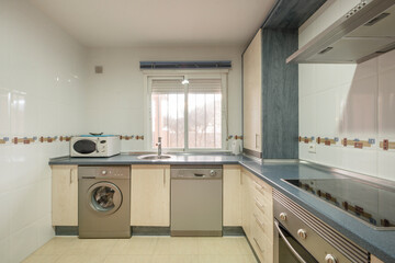 Front image of a kitchen with wooden furniture, integrated stainless steel appliances, white aluminum sash window, microwave oven and blue countertop