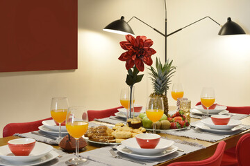 long wooden dining table with designer chairs upholstered in red fabric, black designer lamp and breakfast with fresh fruits and glasses of juice