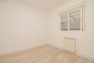Empty living room with light wooden floorboards, white radiator on the wall and sliding sash window
