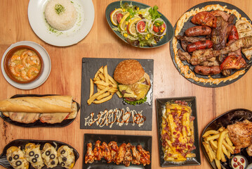 Set of plates of food cooked in the oven with a central tray of assorted roast meat, charcoal-grilled chicken, wings with buffalo sauce, salads and potatoes with cheese and bacon