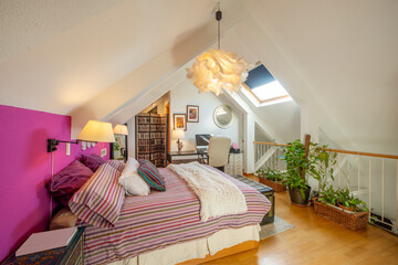 Bedroom with king size bed with cushions and pillows, violet wall to match the duvet and sloping ceilings with skylights