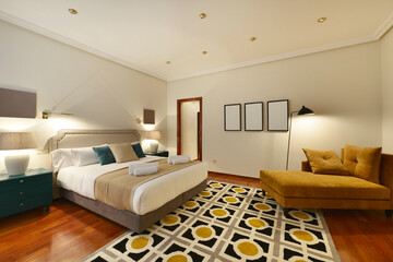 Bedroom with a king-size bed with cushions and pillows, blue bedside tables, mustard-colored velvet...