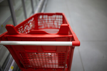 Supermarket aisle with empty red shopping cart with customer defocus background