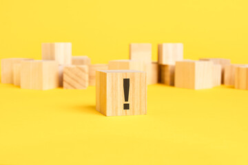 wooden block with exclamation mark sign on a wooden block on a yellow background with copy space. black symbol