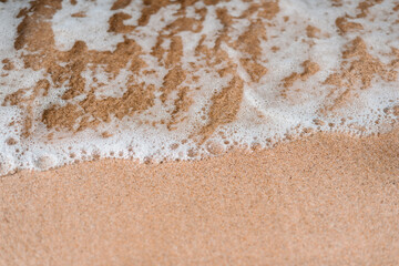 A foamy wave washes ashore on peachy sand with room for text