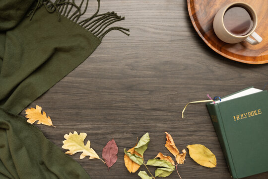 frame of bible, cup of coffee on a wood tray, cozy green blanket and colourful autumn leaves on a dark wood background with copy space