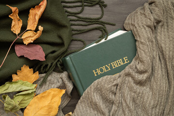 Closed Christian bible with green blanket and autumn leaves on a dark wood background